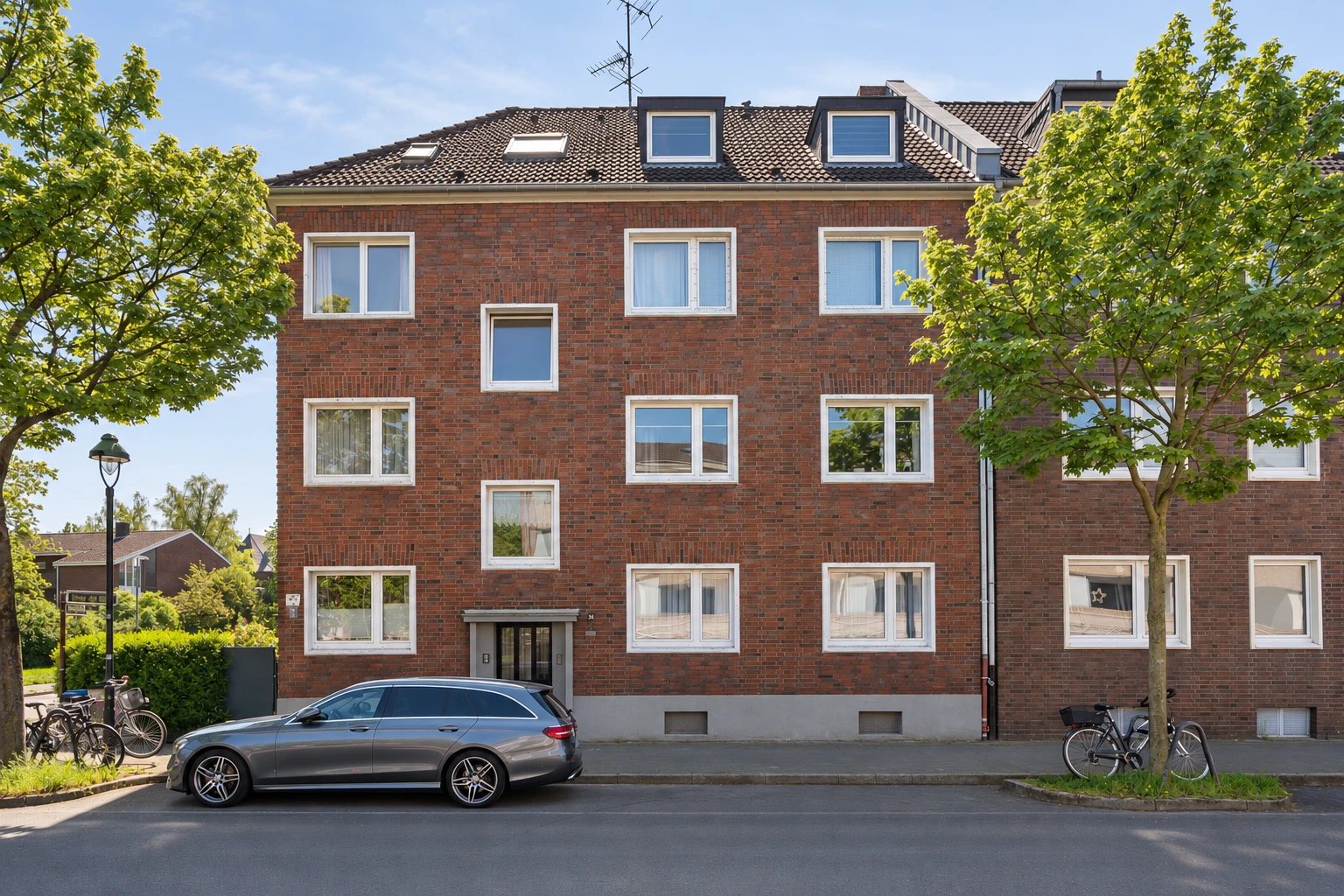 Mehrfamilienhaus mit Klinkerfassade und Bäumen an der Straße