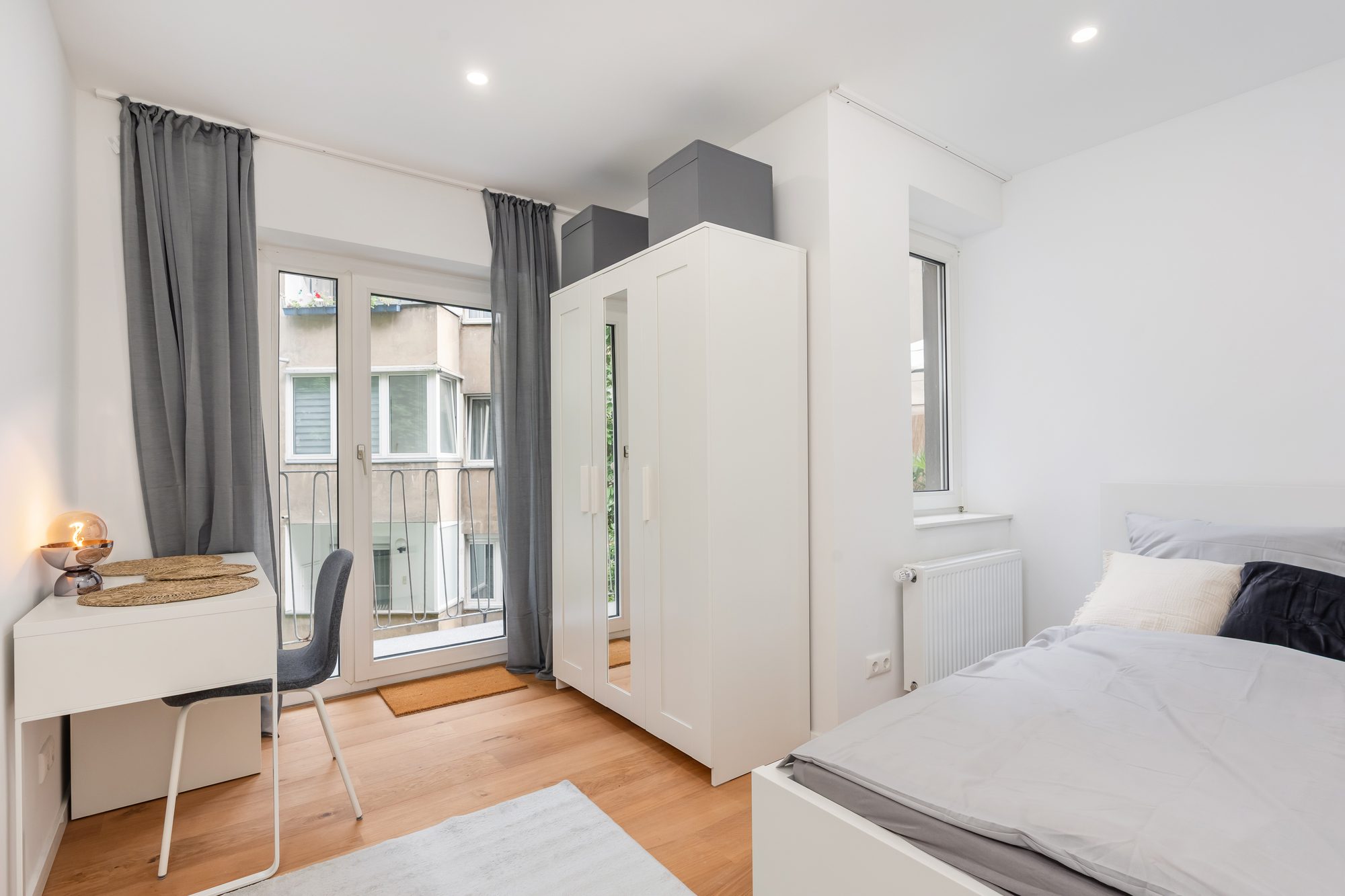 Möbliertes Zimmer mit Balkontür, Bett und Schreibtisch