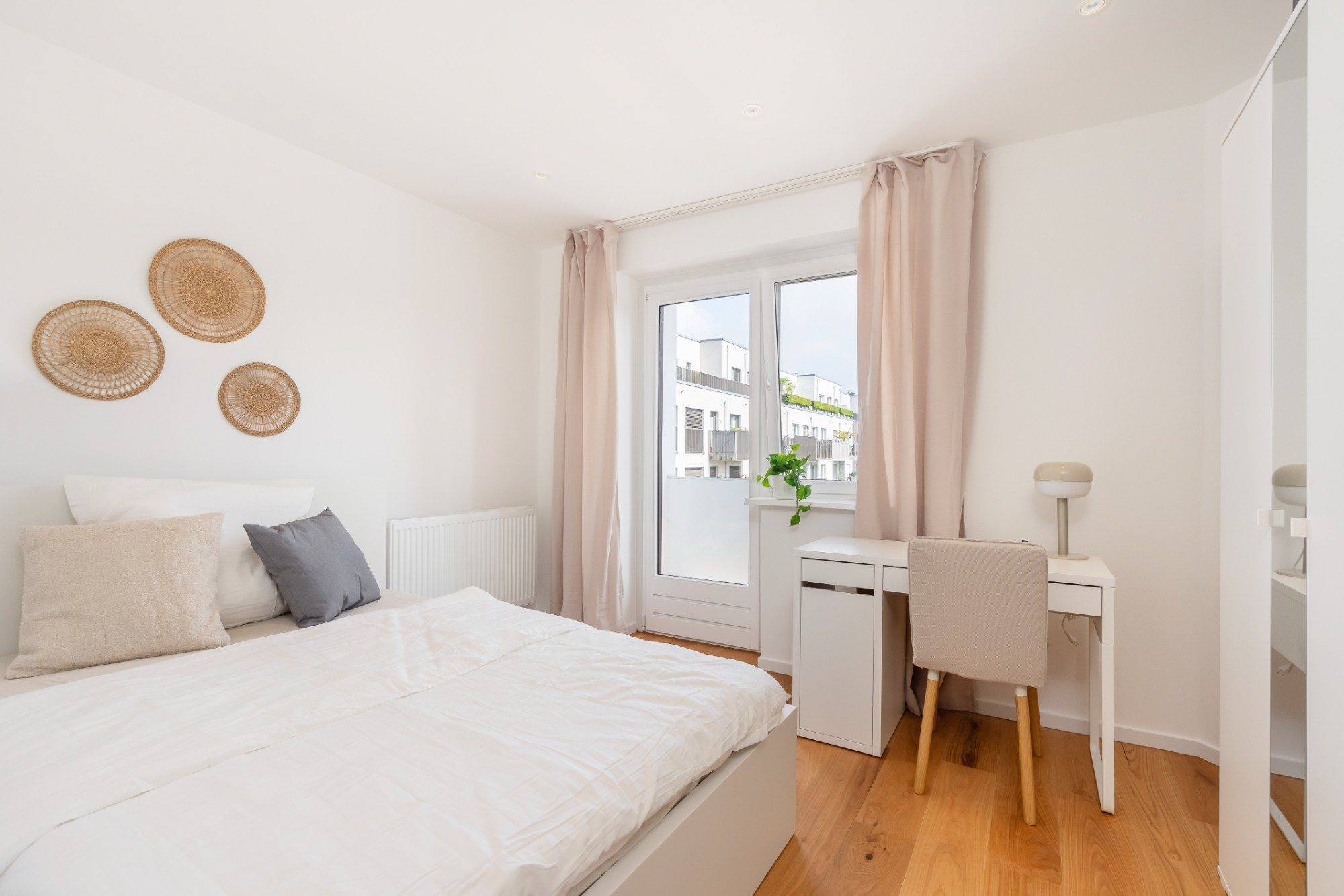 Helles Zimmer mit Bett, Schreibtisch und Tür zum Balkon